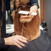 hairdresser-cuts-red-hair-tips-holding-lock-of-red-hair-between-fingers-in-beauty-salon-getting-rid-of-split-ends_Easy-Resize.com